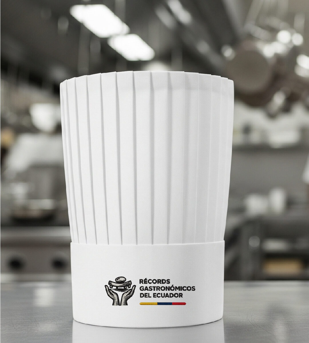 Toque blanco de chef con el logo de Récord Gastronómicos del Ecuador, mostrando la piedra de moler alzada por unas manos y la bandera nacional.