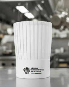 Toque blanco de chef con el logo de Récord Gastronómicos del Ecuador, mostrando la piedra de moler alzada por unas manos y la bandera nacional.